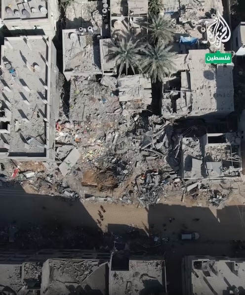 A screenshot of aerial footage showing an airstrike crater and surrounding destruction.