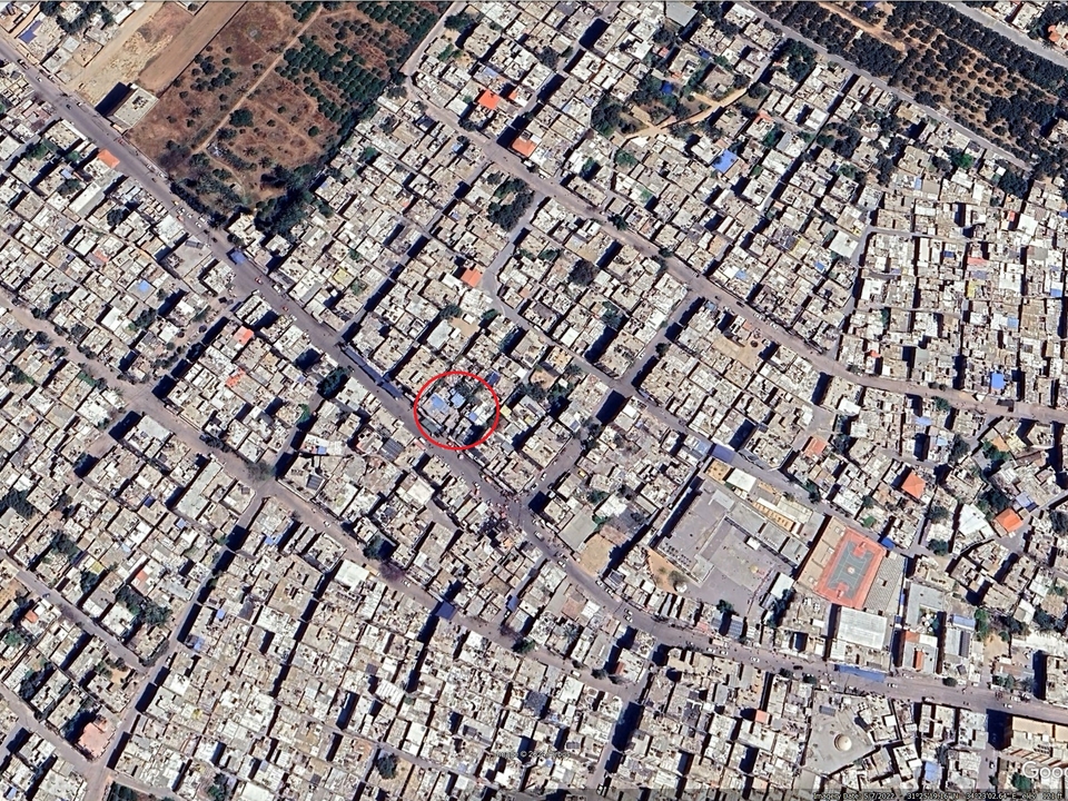 A satellite image of a dense urban area with a red circle around a specific building.